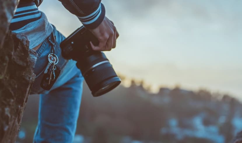 man holding a camera in front of a mountain